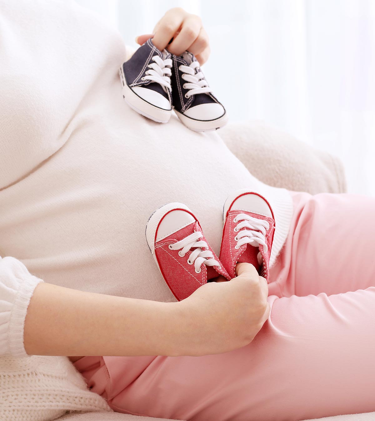 Pregnant women showing two baby shoes for twins